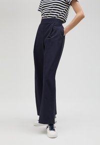 Navy wide-leg trousers with front pockets, smooth texture, high waist, and a clean design, paired with white sneakers.