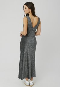 Robe grise sans manches avec un dos en V profond, un corsage ajusté et une jupe évasée. Réalisée dans un tissu scintillant, associée à des baskets blanches.