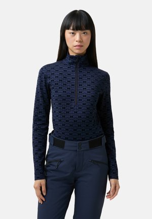 Marineblaues Langarmshirt mit hohem Kragen, das ein strukturiertes Muster ineinandergreifender Formen zeigt; kombiniert mit marineblauen Hosen mit Reißverschlusstaschen.
