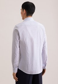 Wit overhemd met blauwe stippen, lange mouwen en een spitse kraag. Voorzien van een gebogen zoom en knoopmanchetten. Gemaakt van lichtgewicht stof.