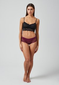 Zwarte kanten bralette met golvende randen, gecombineerd met een bordeauxrode onderbroek met kanten accenten. Beide hebben een zachte textuur en een aansluitend ontwerp.