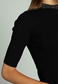 Top corto nero con maniche corte, caratterizzato da un colletto testurizzato con decorazioni. Il tessuto appare liscio e aderente, con un design pulito e strutturato.