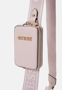 Lyserød læder mini taske med guldfarvet hardware, med "GUESS" logoet, lynlås lukning og en justerbar rem i matchende farve.