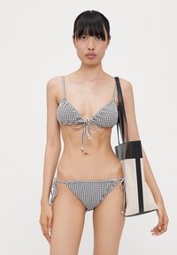 Bikini en vichy noir et blanc avec un haut triangle et un bas à liens sur les côtés. Inclus un sac fourre-tout beige et noir avec des bretelles ajustables.