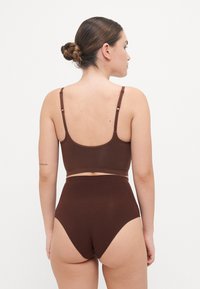 Bralette in cotone marrone con spalline regolabili e slip a vita alta coordinati, caratterizzati da una texture morbida e un design senza cuciture.