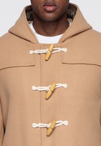Beige duffelcoat med huva, med träknappar och snörstängning, texturerat tyg och platta framfickor.