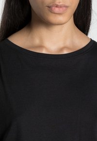 T-shirt nera in cotone con collo rotondo, maniche corte, texture liscia e dettagli di cucitura minima lungo il colletto.