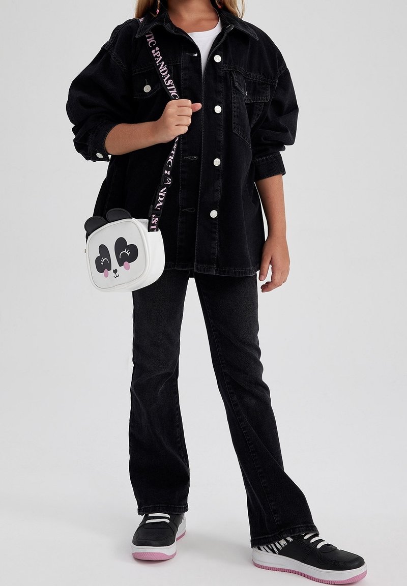 Chaqueta oversized de mezclilla negra con botones blancos, combinada con jeans negros acampanados y zapatillas negras con suelas rosas. Bolso cruzado blanco con diseño de panda.