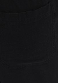 Sort denimstof, der viser en nærbillede af en lomme med en tekstureret overflade og syningsdetaljer. Enkelt design, ingen mønstre eller accenter.