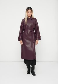 Long, double-breasted coat in a rich purple faux leather, featuring a belted waist, wide sleeves, and circular button details.