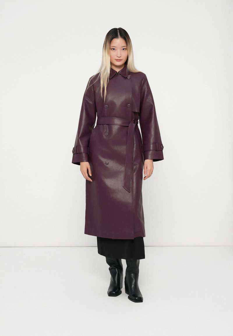 Long, double-breasted coat in a rich purple faux leather, featuring a belted waist, wide sleeves, and circular button details.
