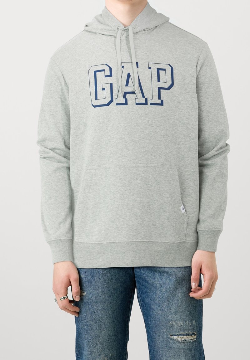 Sudadera con capucha gris hecha de tela suave con un bolsillo tipo canguro. Presenta un gran logo azul "GAP" en el pecho. Los puños y el dobladillo son acanalados.