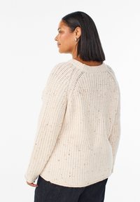 Bežový pletený sveter s voľným strihom, ryhovanou textúrou a bočnými rozparkami. Okrúhly výstrih a dlhé rukávy s uvoľneným dizajnom.