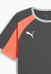 Camiseta deportiva gris con paneles de malla naranja, cuello redondo y un logo blanco. La tela tiene una textura suave con elementos transpirables.
