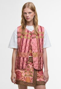 Colete acolchoado em tons de rosa e terrosos com padrão de diamante, apresentando um decote em V, fecho de botão e combinado com uma saia bordada com flores.