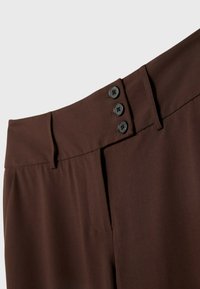 Bruna byxhögmidjade byxor i slät tyg, med platt framstycke, sidoficka och tre svarta knappstängningar vid midjan.
