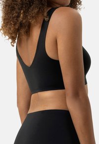 Zwarte sportbeha met brede banden, een V-vormige achterkant, naadloos ontwerp en een gladde textuur. Gecombineerd met bijpassende zwarte onderkleding.