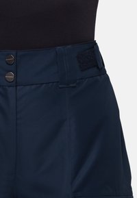 Marinblå shorts med en mjuk textur, utformade med två metallknappar och ett kardborrband i midjan för justerbar passform.
