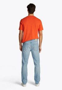 Tricou bărbătesc portocaliu, cu mâneci scurte, material din bumbac; blugi din denim albastru deschis, croială personalizată, două buzunare în partea din spate, cusături texturate. Adidași albi.