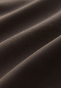 Ruskea kangas, jossa on sileä pinta, hienovaraiset laskokset ja hieno kudontakuvio, korostaen syvyyttä ja varjoja.