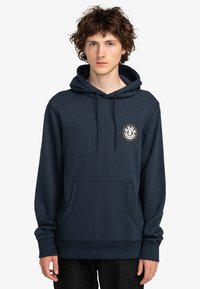 Námornícky modrá mikina vyrobená z mäkkej látky, s klokankovou kapsou, sťahovacou kapucňou a kruhovým logom na hrudi.