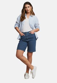 Denim bermuda shortsit korkealla vyötäröllä, yhdistettynä vaaleansiniseen raidalliseen napilliseen paitaan valkoisen t-paidan päällä. Valkoiset lenkkarit viimeistelevät ilmeen.