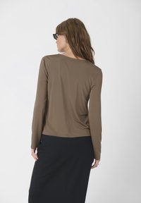 Haut marron à manches longues en tissu doux, avec un col rond, une légère draperie et une coupe décontractée, associé à une jupe noire.