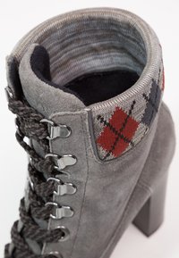 Bottine en suède grise avec un motif argyle tricoté gris, rouge et noir au niveau du haut. Comprend des œillets métalliques et un talon épais.