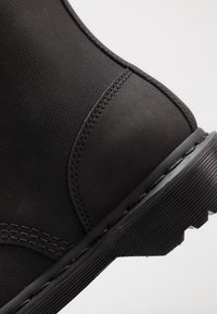 Zwarte enkellaars met een gestructureerd bovenwerk, gladde leren accenten, een stevige rubberen zool met geribbelde details en gestikte naden voor duurzaamheid.