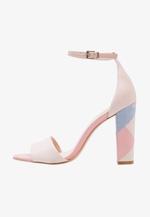 Sandalia de tacón alto en beige con tiras texturizadas, punta abierta y correa en el tobillo. El tacón cuadrado presenta un patrón geométrico en tonos pastel de rosa, azul y beige.