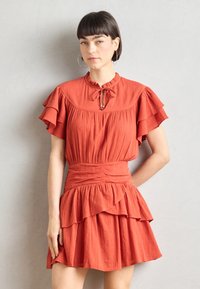 Rochie de culoare ruginie cu mâneci scurte și volănașe, decolteu tip cheie și talie ajustată, având volane stratificate și material texturat.