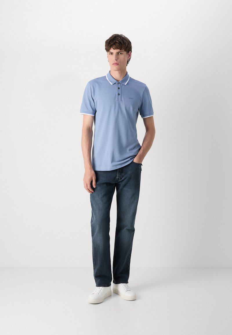 Polo bleu clair avec un col, trois boutons et des finitions blanches, associé à un jean en denim foncé et des baskets blanches.
