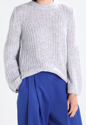 Suéter de punto gris con canalé, cuello redondo y mangas sueltas, combinado con pantalones azul de cintura alta. Textura suave y corte relajado.
