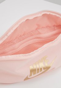 Růžová textilní taštička se zlatým logem "Nike", s mřížkovanou vnitřní částí a hladkým povrchem, navržená s otevíráním na zip.