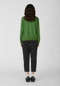 Groen lichtgewicht sweatshirt met boorden, gecombineerd met zwarte taps toelopende jeans en stevige zwarte schoenen, gezien vanaf de achterkant.