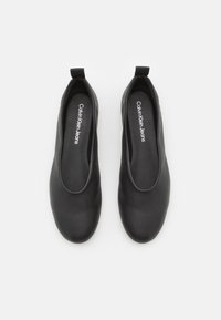 Crne cipele bez kopčanja izrađene od glatkog sintetičkog materijala. Imaju zaobljen vrh i minimalistički dizajn s logotipom "Calvin Klein Jeans" unutar cipele.
