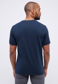 Tamsiai mėlyna trumpomis rankovėmis marškinėliai, pagaminti iš minkštos medvilnės, su klasikiniais apvaliais iškirpimais ir laisvu siluetu, su diskretiškomis siūlių detalėmis.