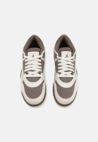 Chaussures de sport marron et blanches avec partie supérieure rembourrée, fermeture à lacets et détail du logo sur la languette ; présentant des superpositions texturées et des panneaux lisses.