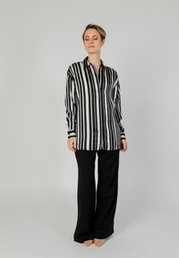 Blusa a righe verticali bianca e nera con chiusura a bottoni, maniche lunghe e vestibilità comoda, abbinata a pantaloni neri a gamba larga e tacchi nudi.