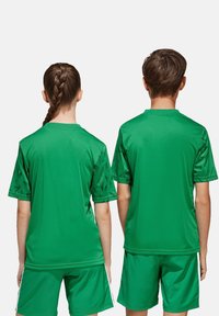 Maglia sportiva verde e pantaloni corti, con maniche testurizzate e un motivo geometrico, realizzati in un tessuto liscio e leggero.