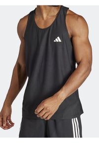 Débardeur de sport noir en tissu respirant, avec un col rond et un logo Adidas blanc sur la poitrine gauche. Texture lisse.