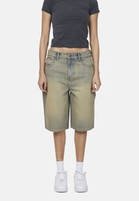 Bermuda shorts in denim di colore azzurro chiaro, dalla vestibilità rilassata, con tasche frontali e vita standard. Abbinati a scarpe da ginnastica bianche e calze.