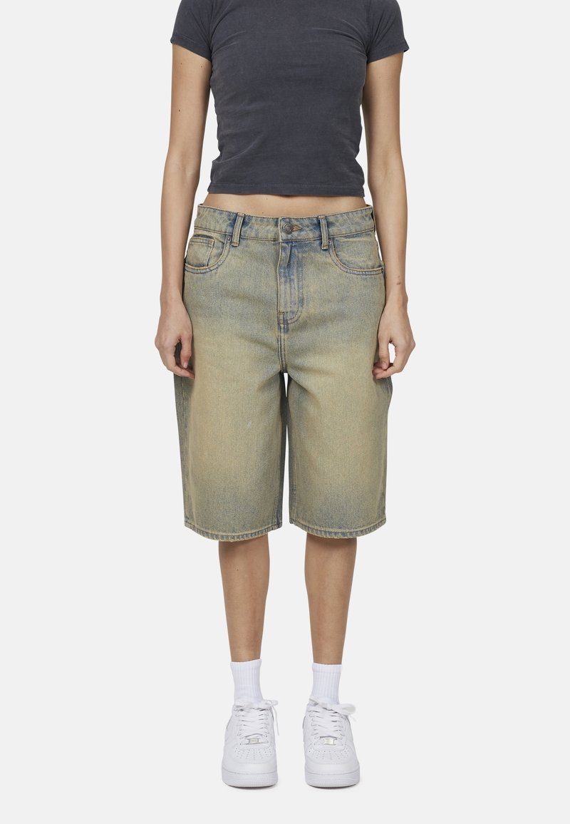 Bermuda shorts in denim di colore azzurro chiaro, dalla vestibilità rilassata, con tasche frontali e vita standard. Abbinati a scarpe da ginnastica bianche e calze.