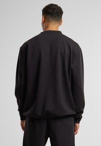 Czarna bluza z okrągłym dekoltem ma obniżone ramiona, miękką teksturę i luźny krój. Ribbed cuffs and hem dopełniają wzór.