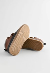 Bruine leren en grijze textiel schoenen met een rubberen zool met een gestructureerd patroon en twee verstelbare bandjes op de bovenkant.