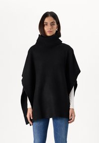 Poncho en tricot noir avec un col roulé haut et côtelé. Comprend des manches larges et une coupe surdimensionnée. Le tissu texturé crée une apparence conviviale.