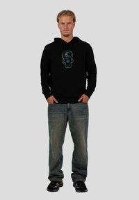 Czarna bluza z kapturem z kolorową postacią z kreskówki na piersi, w połączeniu z jasnoniebieskimi dżinsami i czarnymi sneakersami.