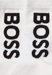 Calcetines blancos con el gran texto negro "BOSS" bordado en los lados. La tela es lisa y suave al tacto, destacando una clara identificación de marca.