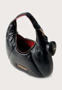 Schwarze Leder-Umhängetasche mit strukturierter Oberfläche, goldenen Beschlägen, rotem Innenfutter mit einem Logomuster und einem herzförmigen Anhänger.