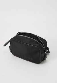 Black nylon crossbody bag with a zip closure, embossed logo, and sleek rectangular design. Includes a side strap and metallic accents.